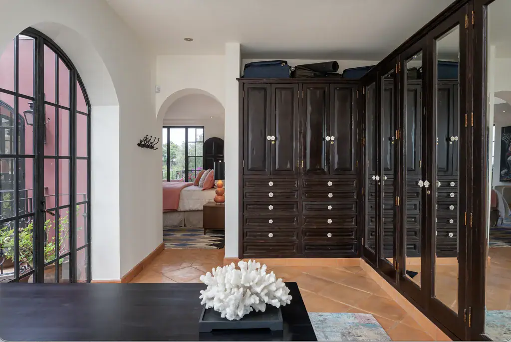 Casa del Arroyo, dressing room with dark wood built-in wardrobes and an arched window, San Miguel de Allende