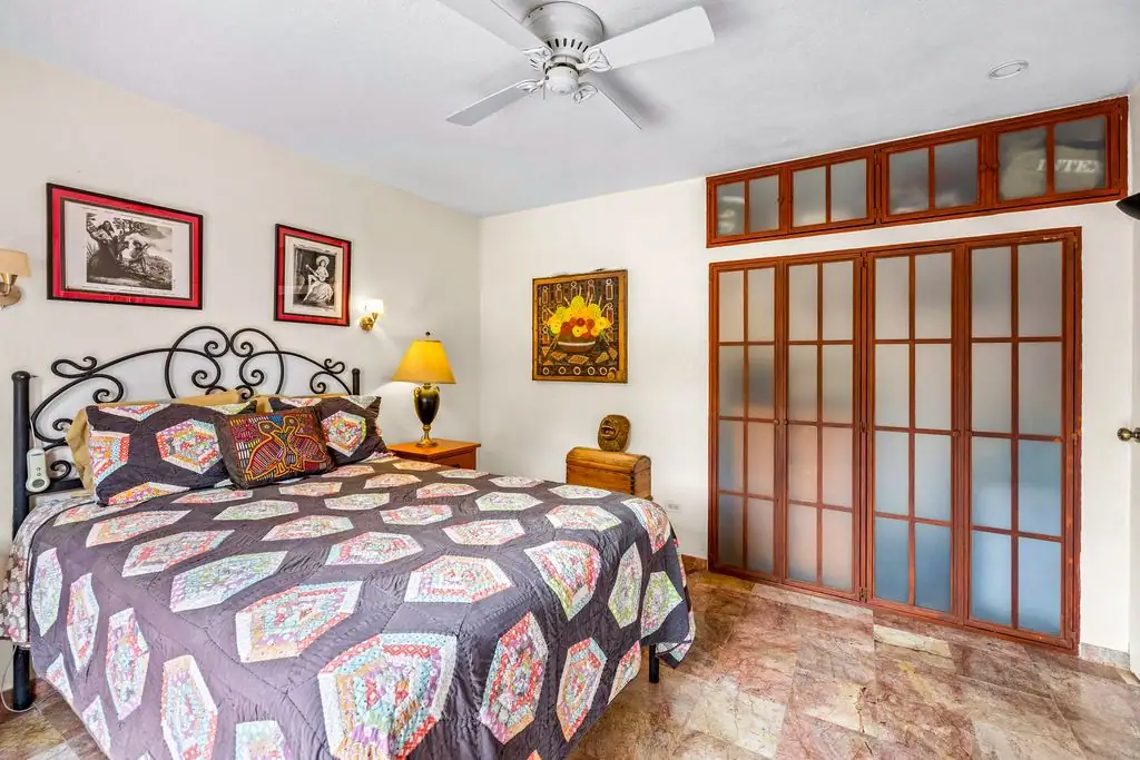 Bedroom with a quilted bed, black wrought-iron headboard, two framed pictures, and frosted glass paneled doors at the end of the room, San Miguel de Allende