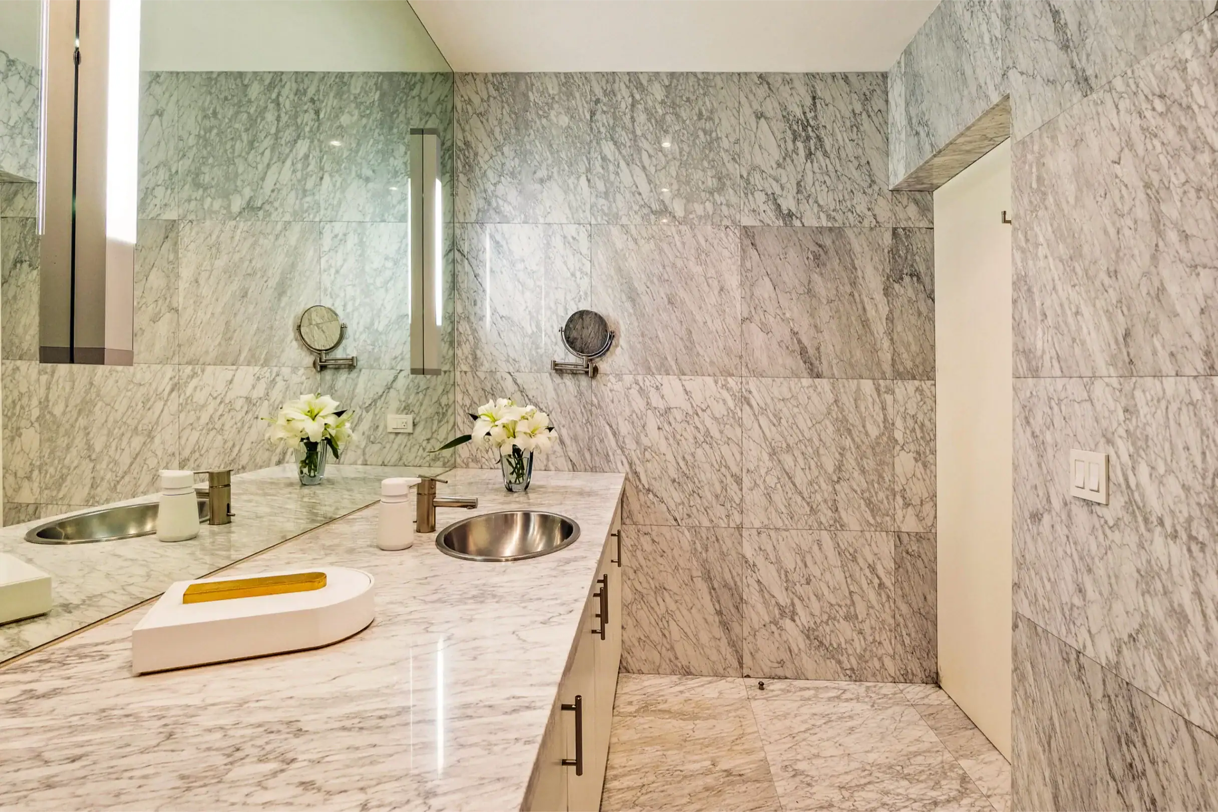 Marble bathroom vanity with two sinks, chrome fixtures, and vases of white flowers on a marble countertop, San Miguel de Allende