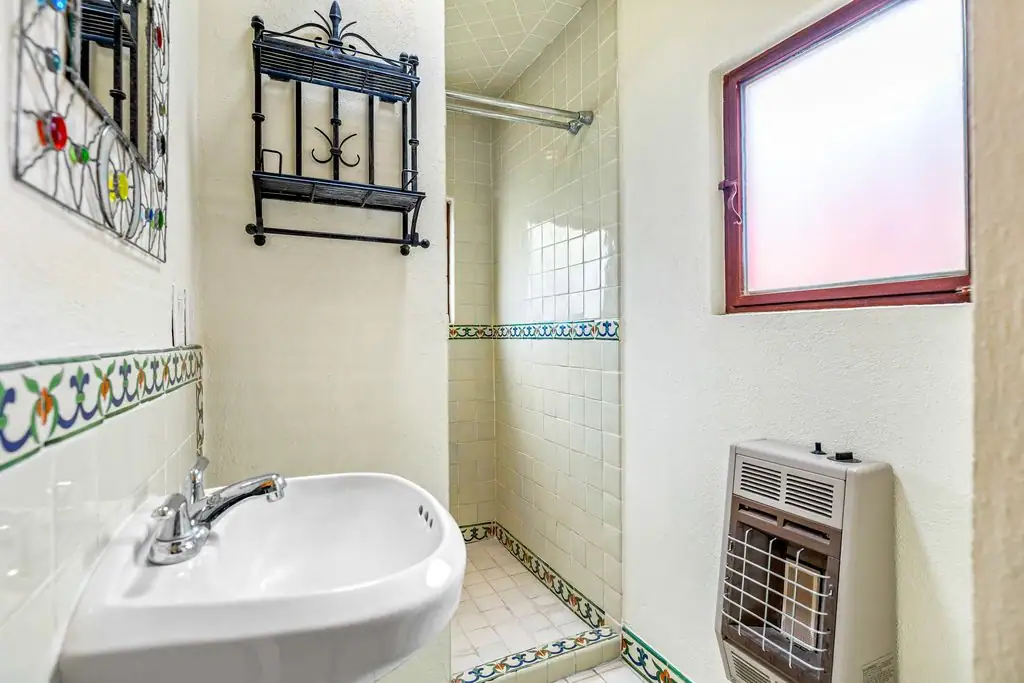 Compact bathroom with a white pedestal sink, frosted window, and open shower stall bordered by decorative tile trim, San Miguel de Allende