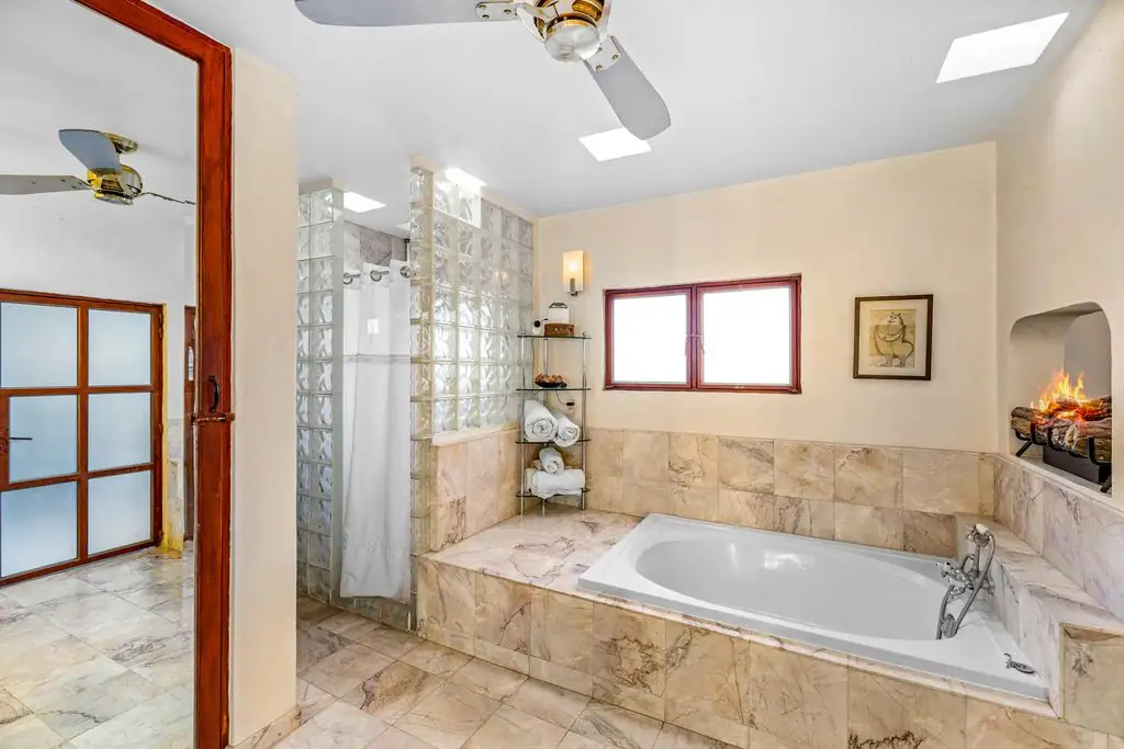 Bright marble bathroom with corner soaking tub, glass block shower, wall fireplace, and skylight windows on the ceiling, San Miguel de Allende