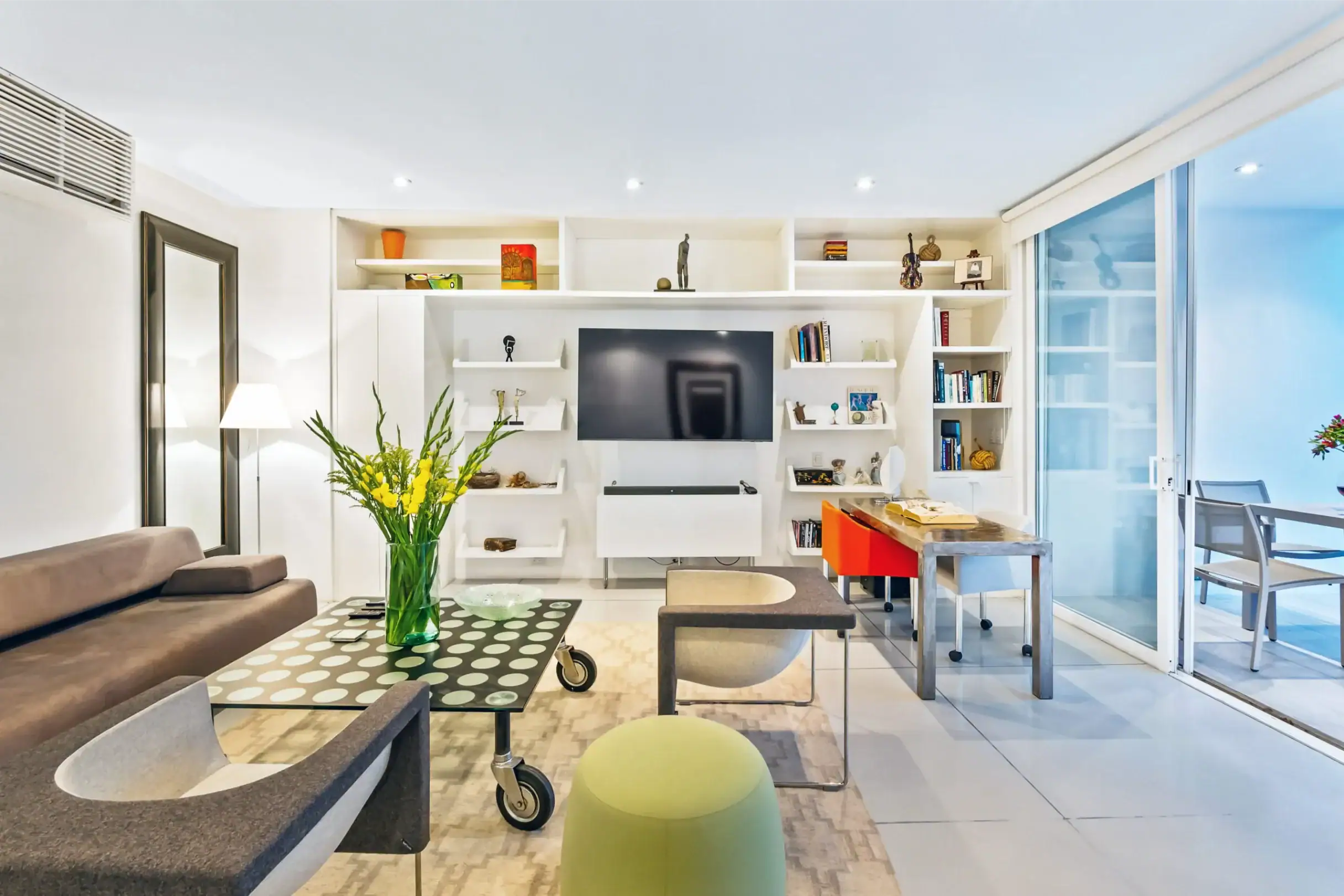 Bright modern living room with white built-in shelves, a wall-mounted TV, and a glass sliding door to an outdoor area on the right, San Miguel de Allende