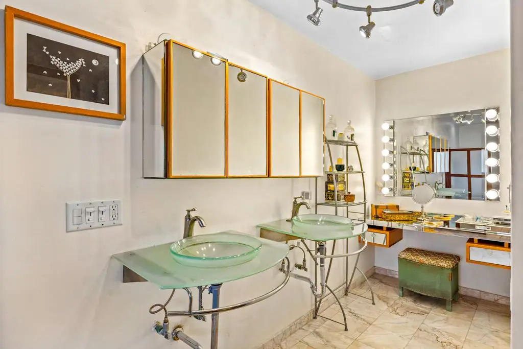 Dual glass vessel sinks on curved metal vanities with a backlit makeup mirror and storage shelves, San Miguel de Allende