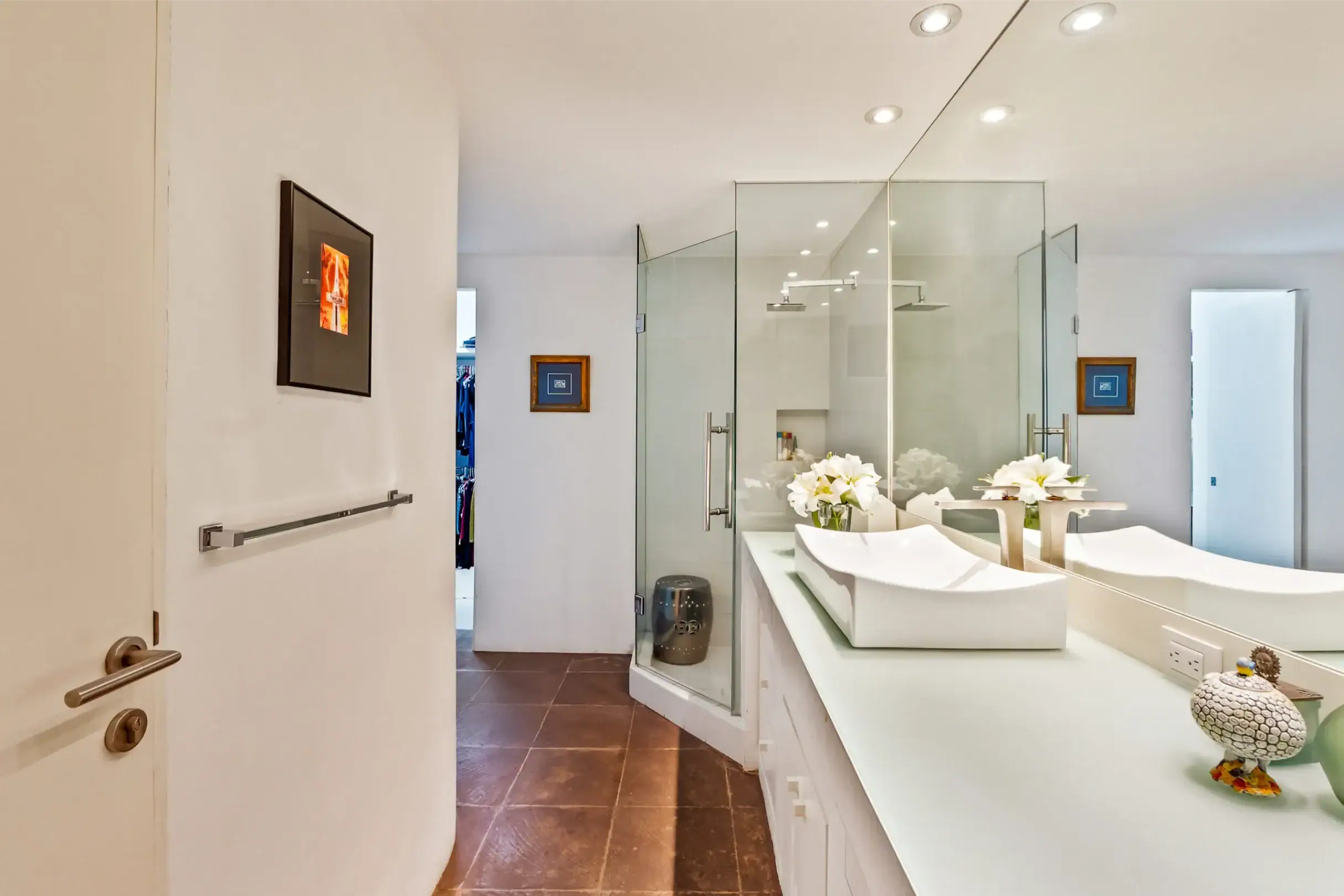 Modern bathroom with a frameless glass shower, dual white vessel sinks on a long counter, and fresh flowers on the countertop, San Miguel de Allende