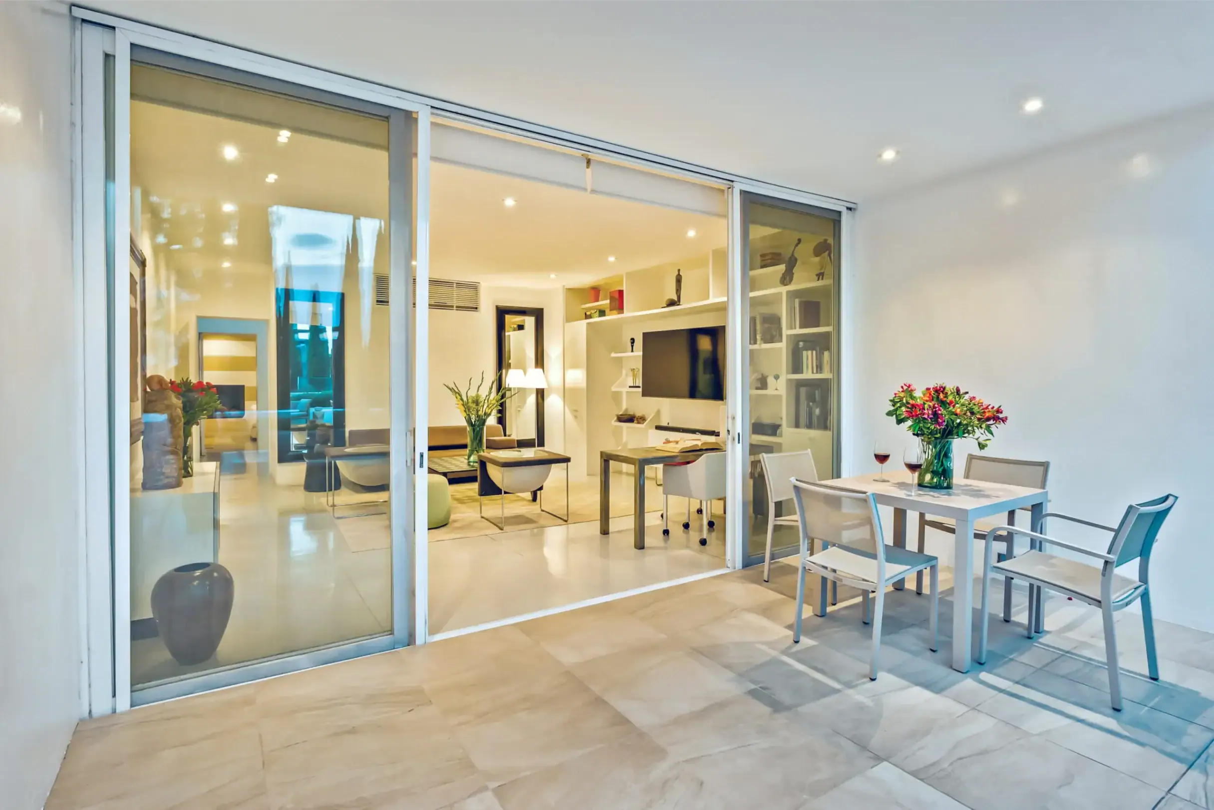 Sliding glass doors open to a bright, modern living and dining area with an outdoor table and flowers nearby, San Miguel de Allende