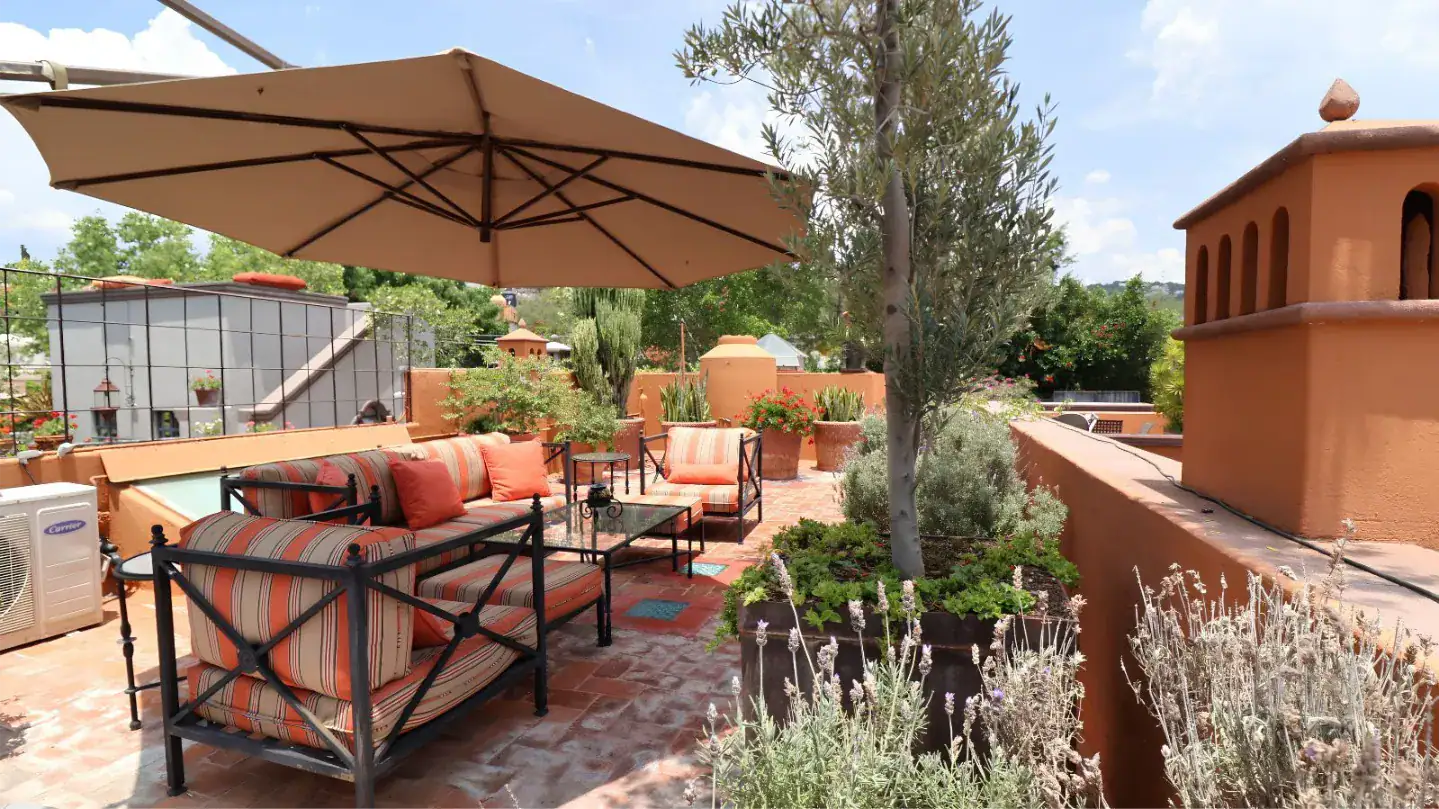 Sunny rooftop terrace with striped-cushion seating, a large beige umbrella, and orange terracotta walls, San Miguel de Allende