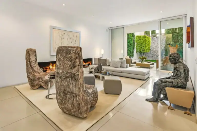 Open, modern living room with sculptural beige chairs, a sleek fireplace, gray sofa, and sliding glass doors to a garden, San Miguel de Allende