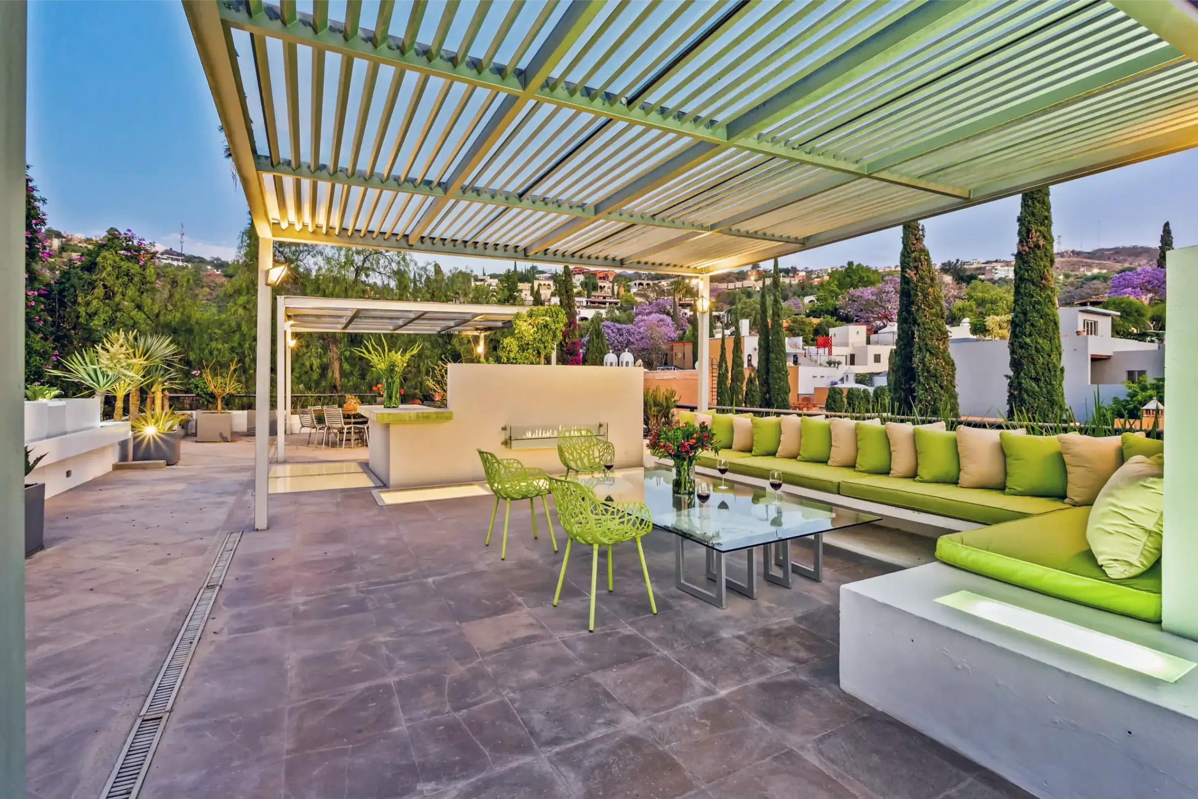 Outdoor patio with lime-green seating under a slatted pergola, hillside in the distance and purple flowering trees farther away, San Miguel de Allende