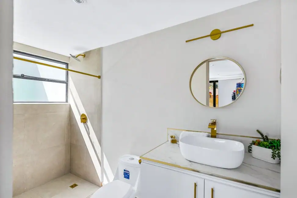 Casa Angel, bathroom with a white vessel sink, round gold mirror and shower, San Miguel de Allende