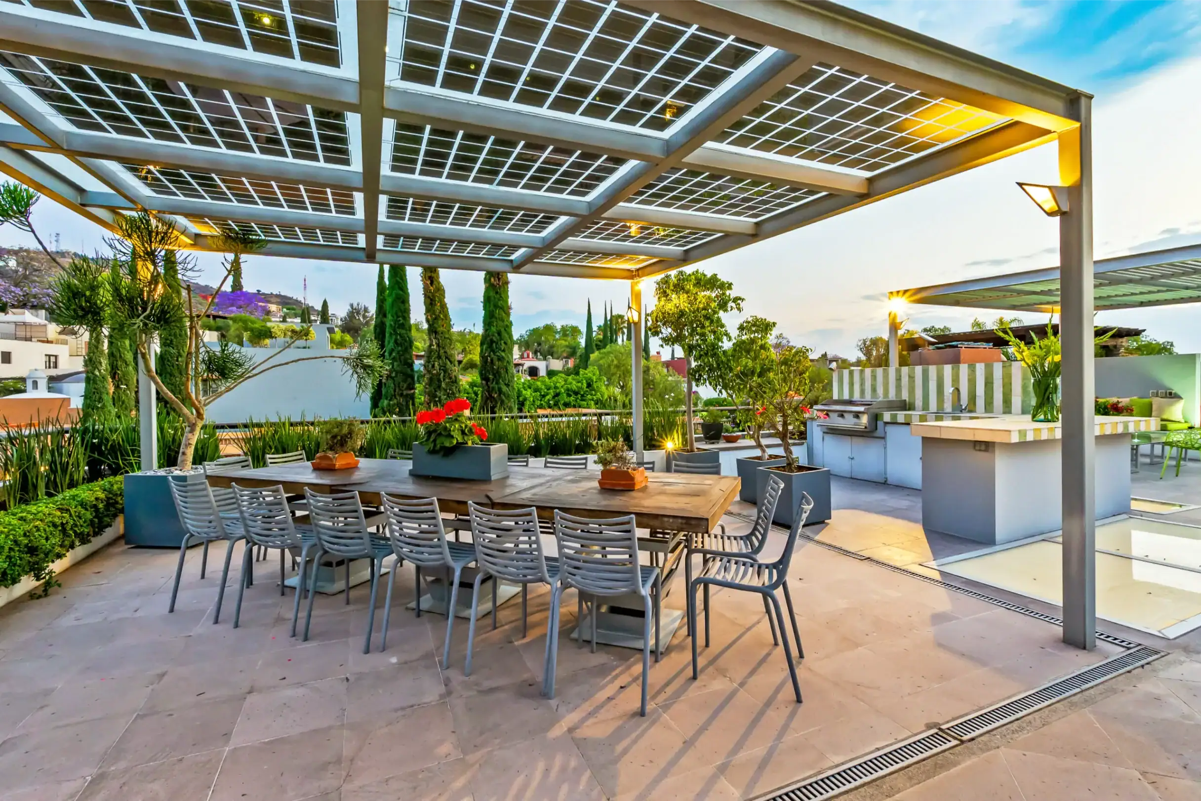 Outdoor dining area under a grid solar pergola with a long wooden table and gray chairs, evening garden lights on, San Miguel de Allende