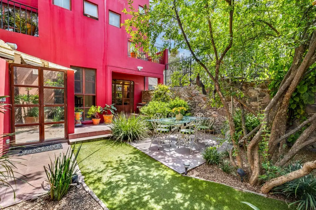 Bright pink courtyard with glass doors, potted plants, and a round metal table set in the shade under trees, San Miguel de Allende