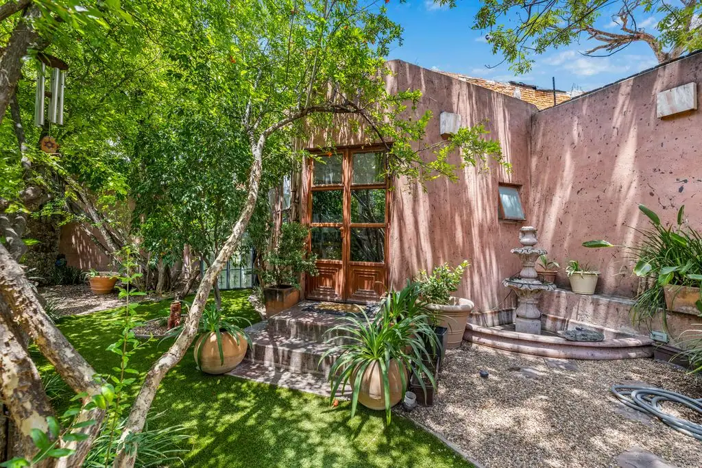 Courtyard with pink stucco walls, wooden door, fountain, and potted plants under leafy trees, San Miguel de Allende