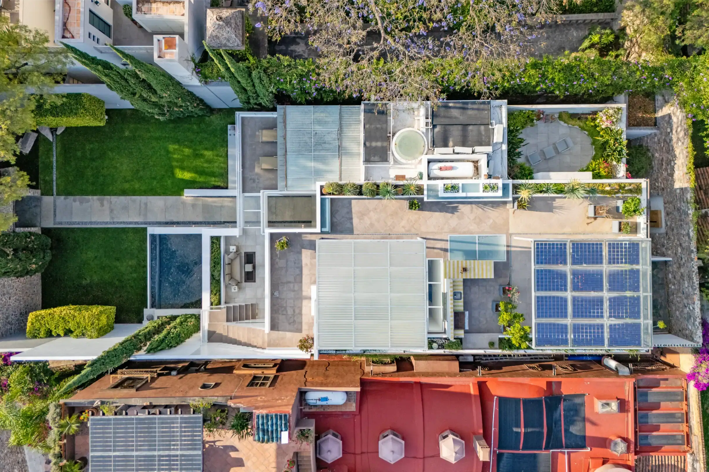 Aerial view of a modern neighborhood with solar panels on flat roofs, green lawns, and outdoor patios surrounding the houses, San Miguel de Allende