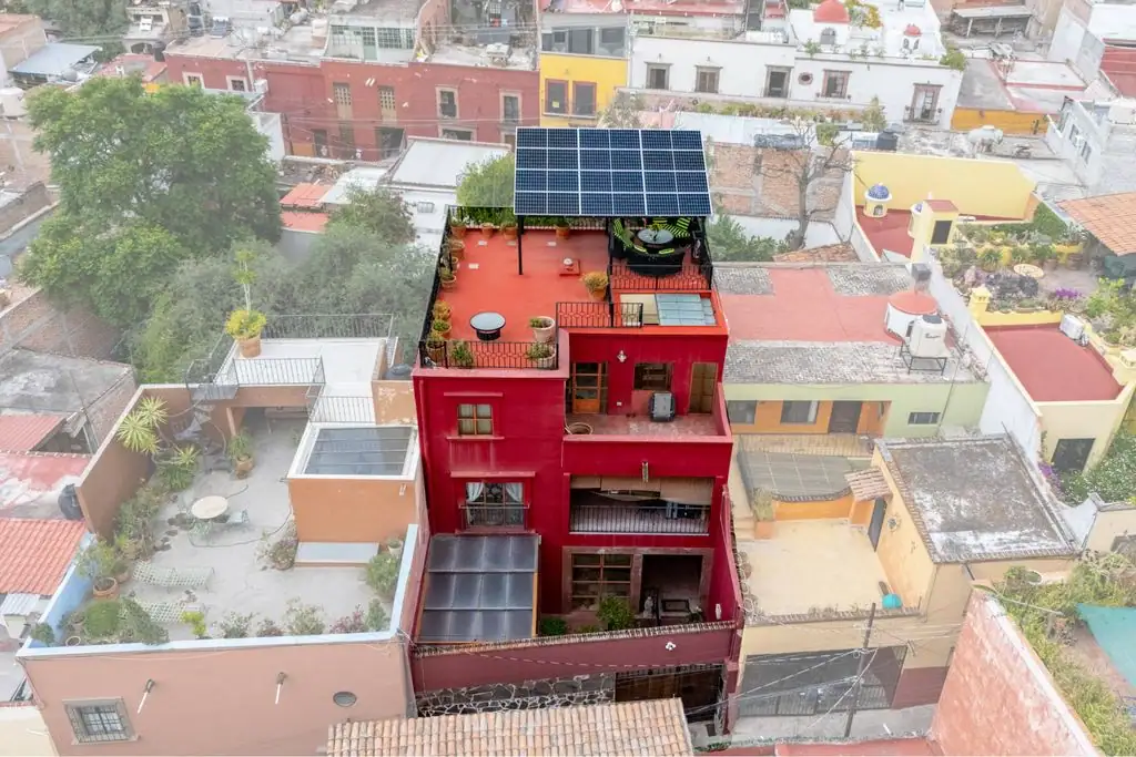 A red multi-story house with a rooftop terrace and solar panels, surrounded by colorful neighboring buildings (aerial view), San Miguel de Allende
