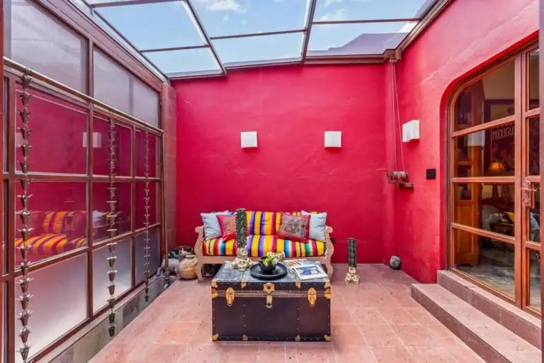 Indoor courtyard with red walls and a glass roof, featuring a colorful striped sofa and a vintage trunk coffee table in the center, San Miguel de Allende