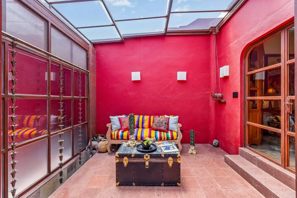 Indoor courtyard with red walls and a glass roof, featuring a colorful striped sofa and a vintage trunk coffee table in the center, San Miguel de Allende