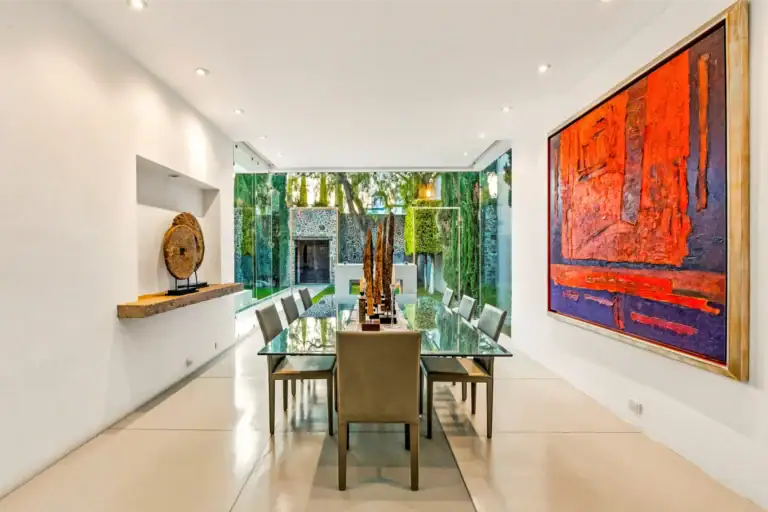 Bright modern dining room with a glass-topped table, grey chairs, and a large red abstract painting on the right; garden view through glass walls, San Miguel de Allende