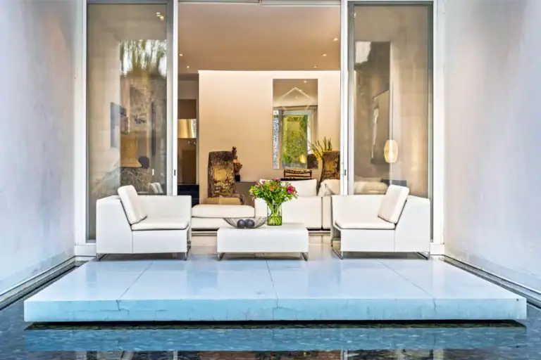 Modern outdoor living room with white cushioned seating around a glass coffee table, opening to an interior space with a blue-tiled pool in the foreground, San Miguel de Allende
