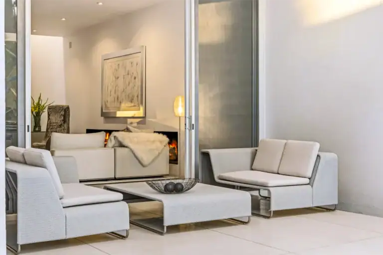 Modern living room with white modular seating, glass coffee table, and a lit fireplace framed by a large doorway, San Miguel de Allende