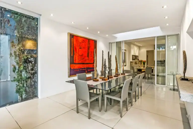 Modern dining room with glass-topped table, grey chairs, red abstract painting, and tall sculptural decor, San Miguel de Allende