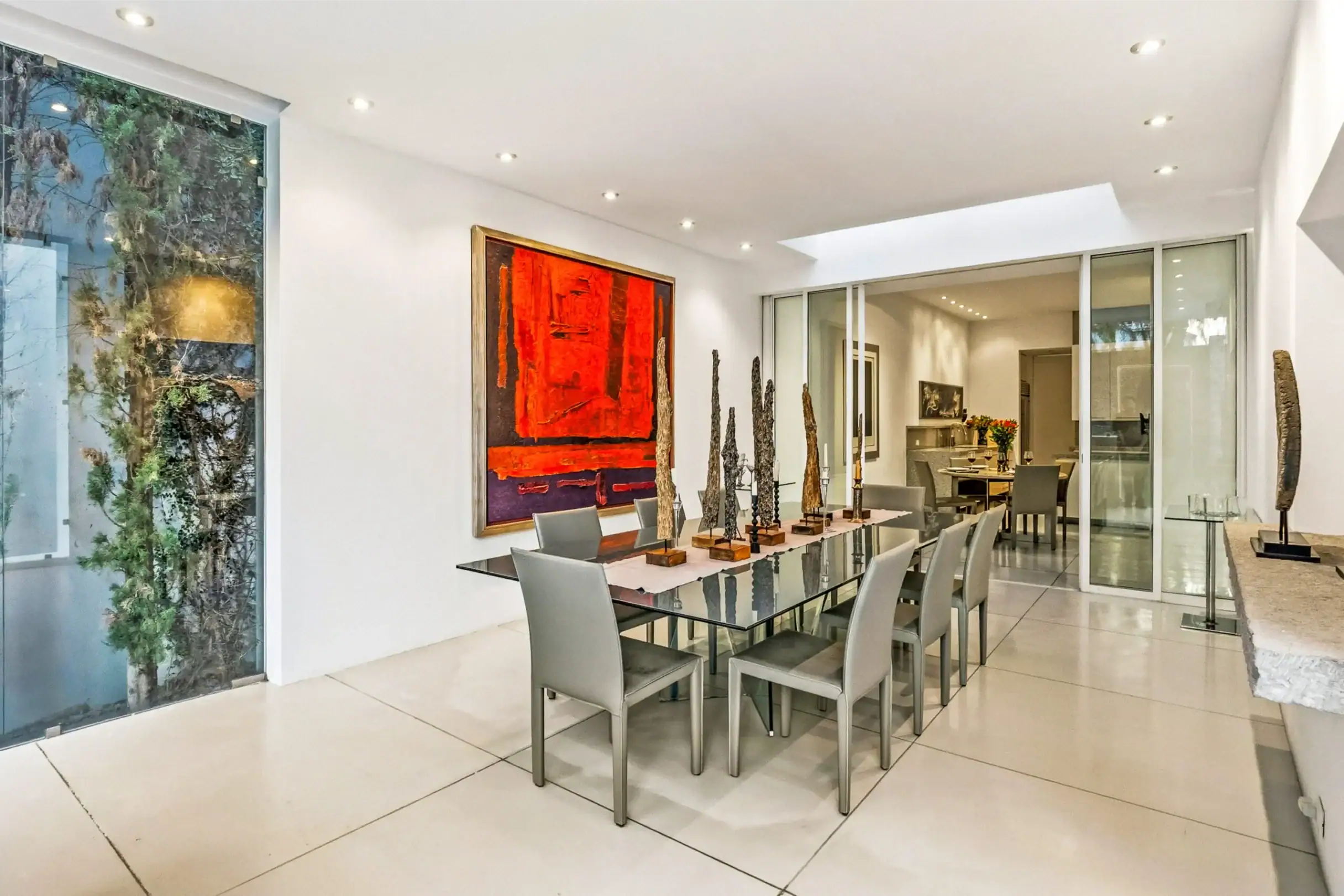 Modern dining room with glass-topped table, grey chairs, red abstract painting, and tall sculptural decor, San Miguel de Allende