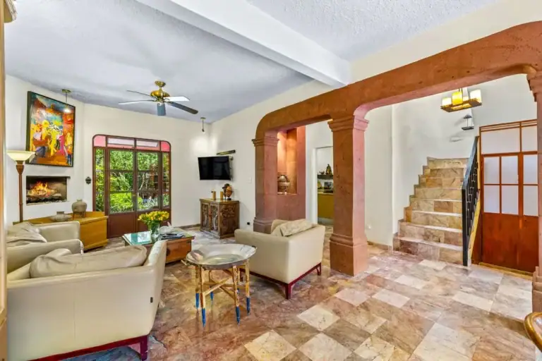 Cozy living room with cream leather sofas, a glass coffee table, and a built‑in fireplace with a colorful painting above it, San Miguel de Allende