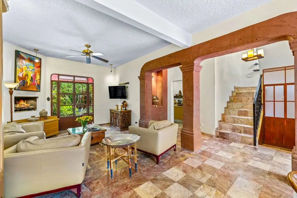 Cozy living room with cream leather sofas, a glass coffee table, and a built‑in fireplace with a colorful painting above it, San Miguel de Allende
