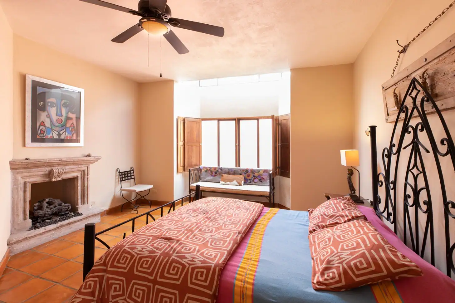 Casa Brillante, bedroom with an iron bed, stone fireplace and ceiling fan, San Miguel de Allende