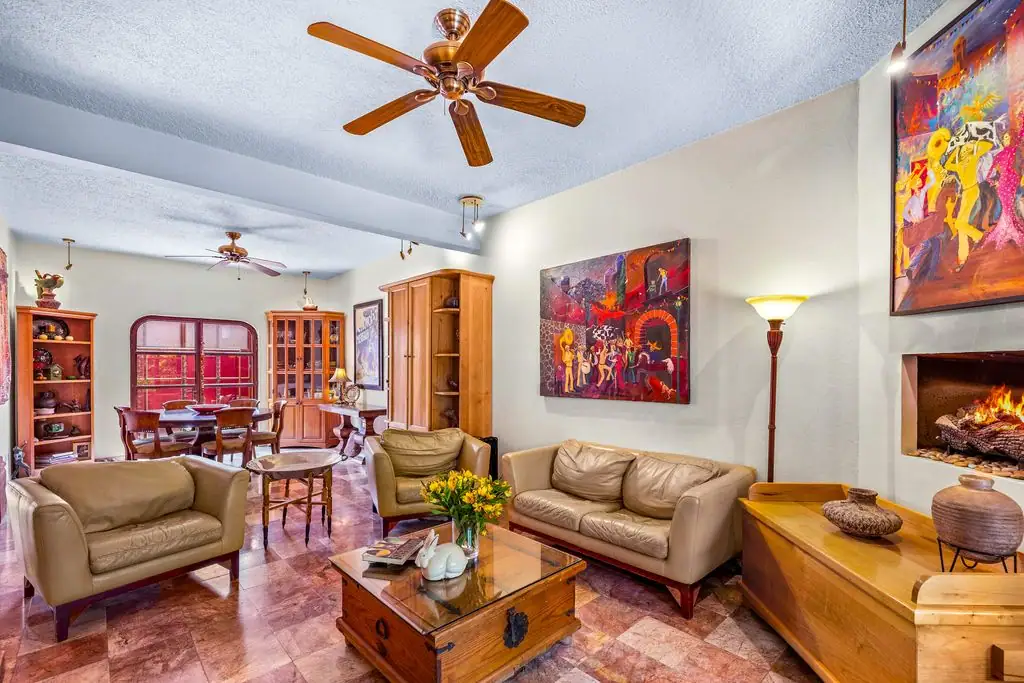 Cozy living room with beige sofas, wooden coffee table, and a lit fireplace, plus colorful wall art and a wooden cabinet in a spacious home interior, San Miguel de Allende