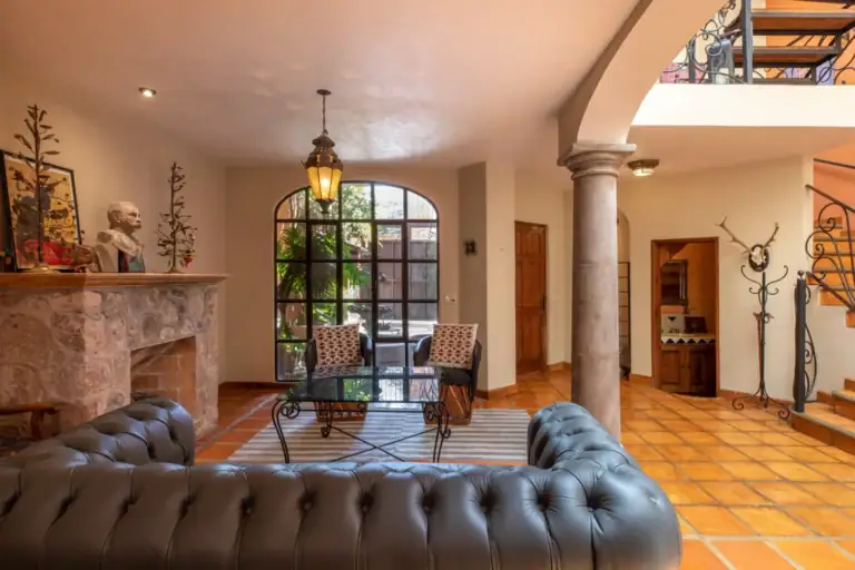 Casa Brillante, living room with a stone fireplace, leather sofa and arched glass doors, San Miguel de Allende