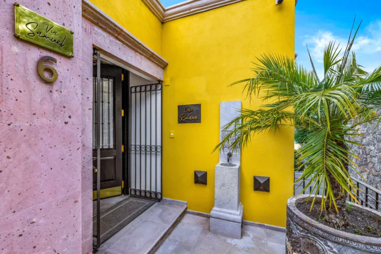 Casa Romana, entrance with a yellow wall, a stone fountain and a palm, San Miguel de Allende