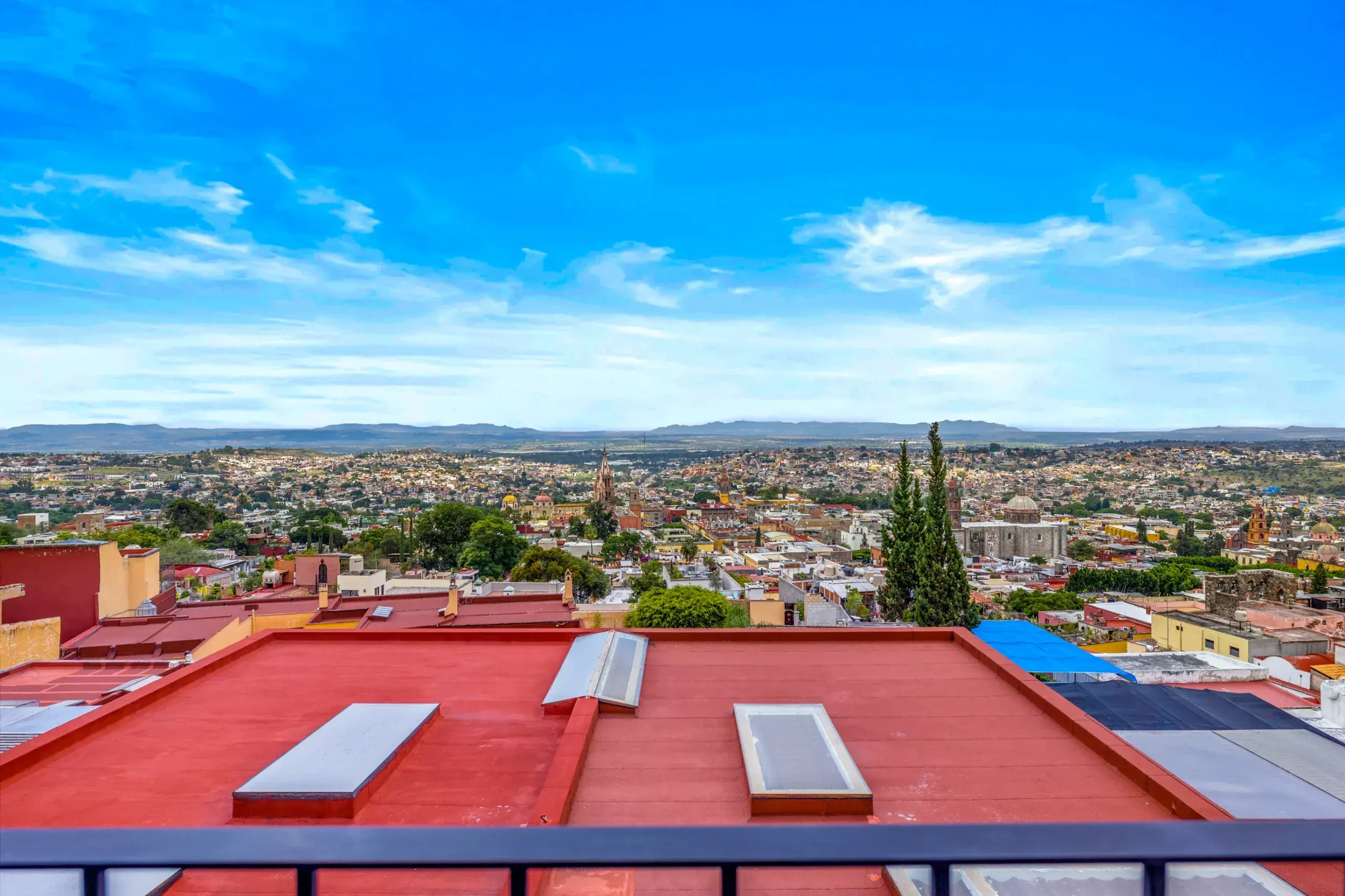 Casa Romana, view across red rooftops to the city under a blue sky, San Miguel de Allende