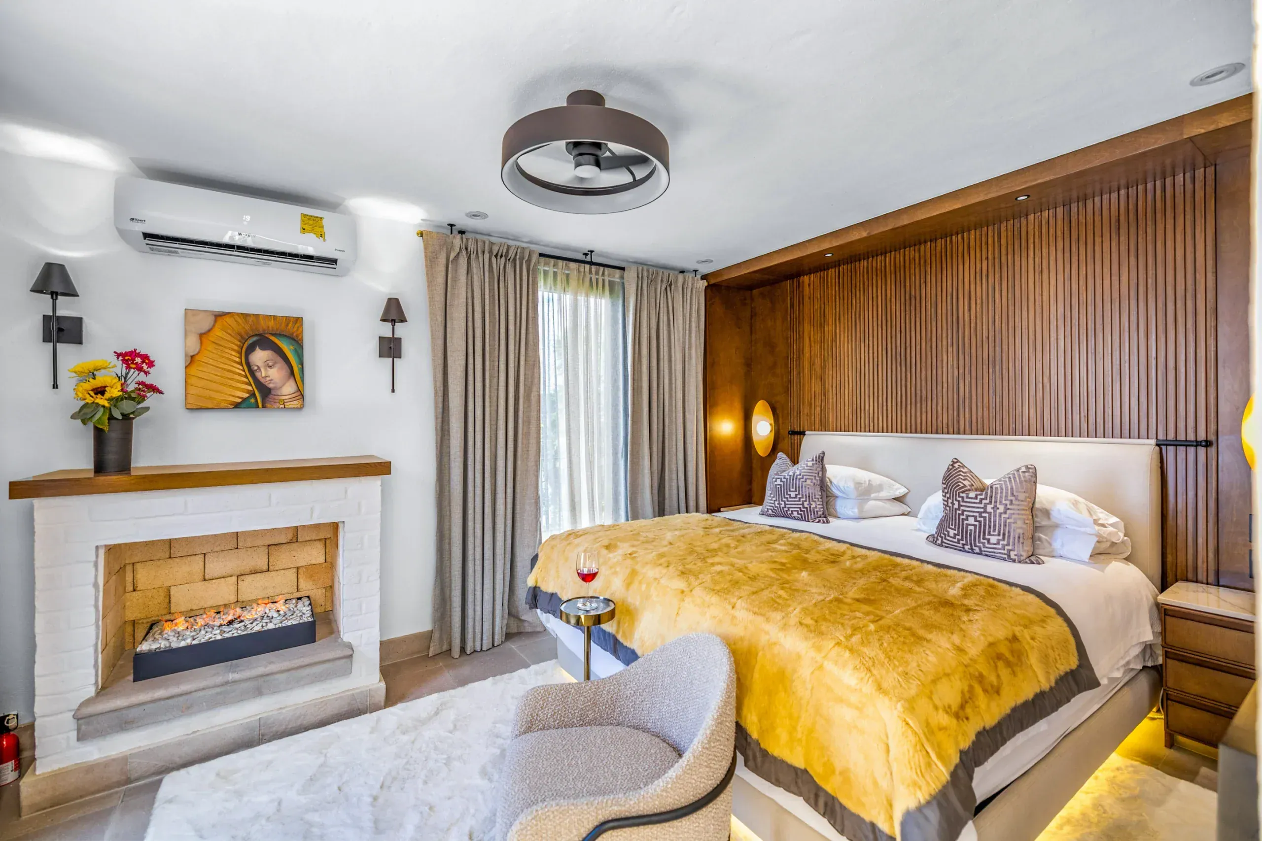Casa Romana, bedroom with a fireplace, a gold bedspread and a wood-paneled headboard wall, San Miguel de Allende