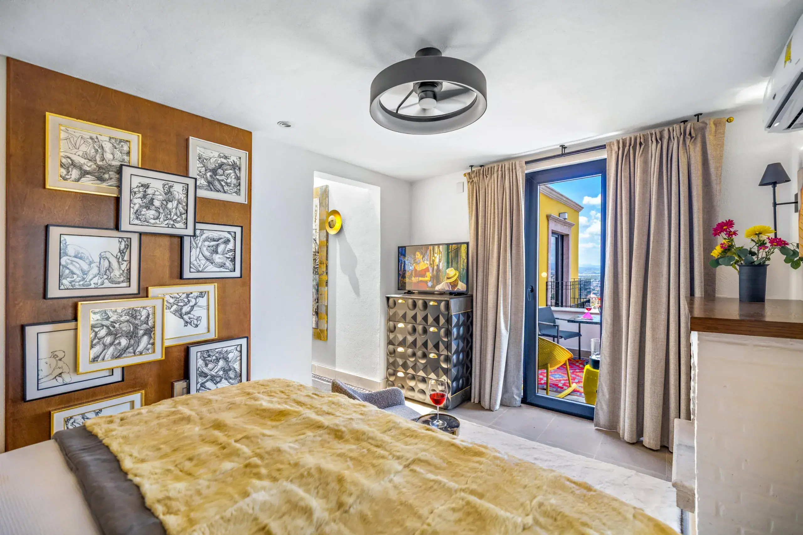 Casa Romana, bedroom with a wall of framed drawings and a balcony door, San Miguel de Allende