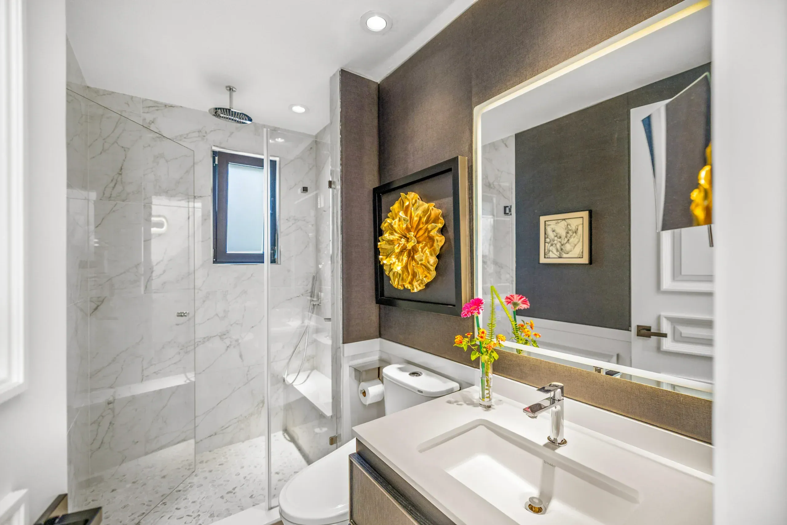 Casa Romana, bathroom with a marble shower, a lit mirror and a gold wall sculpture, San Miguel de Allende