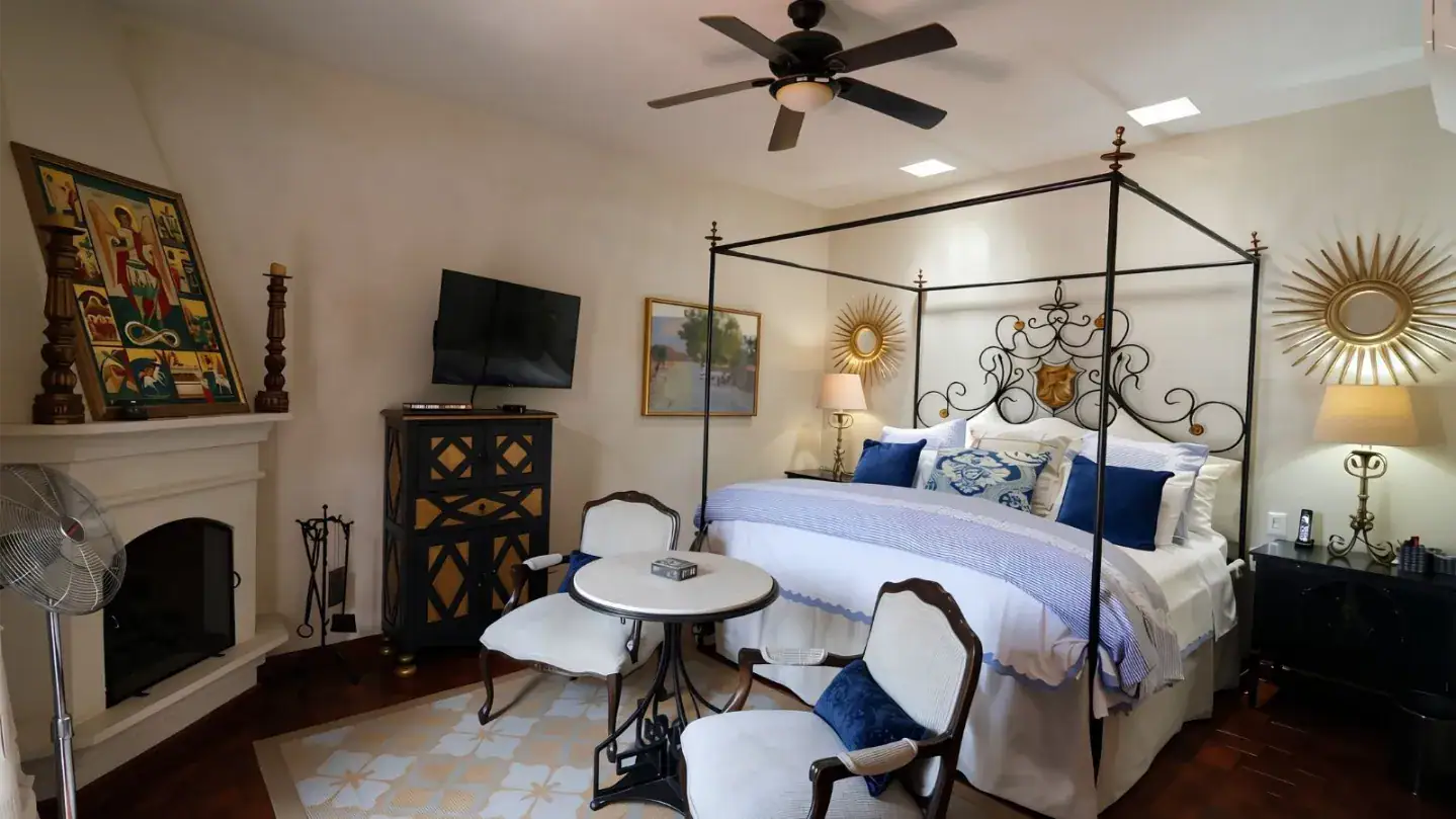 Elegant bedroom with a black wrought-iron four-poster bed, blue-and-white bedding, and sunburst mirrors on the wall, San Miguel de Allende