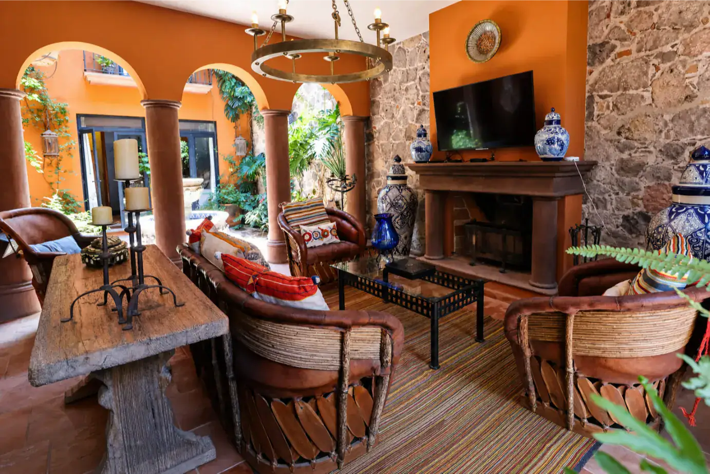 Cozy Mediterranean living room with orange arches, stone walls, wicker seating, and a stone fireplace with TV above it, San Miguel de Allende