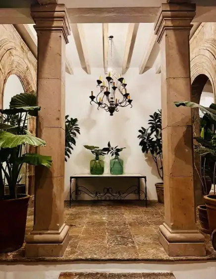 Decorative entryway with stone columns, a wrought-iron chandelier, and potted plants flanking a console table, San Miguel de Allende