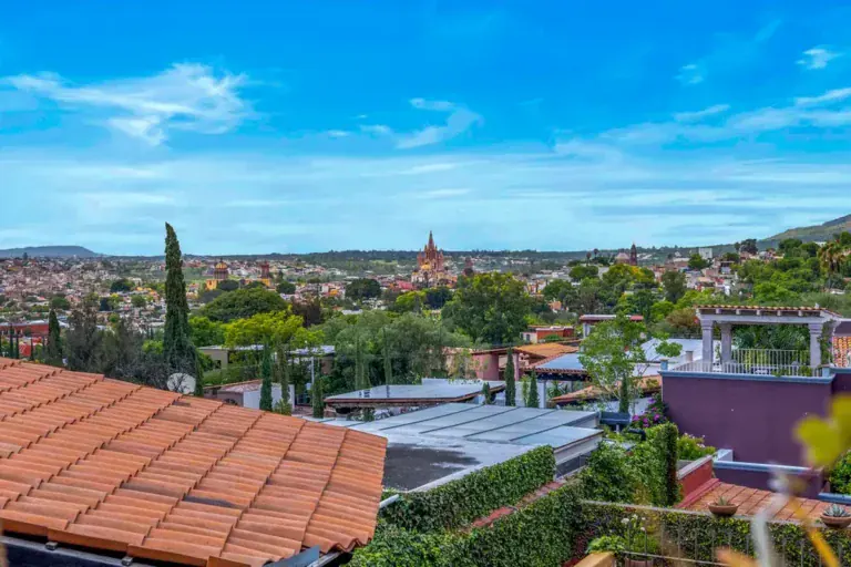 Terracotta tile roof in the foreground with city views and the parish church tower in the distance, San Miguel de Allende