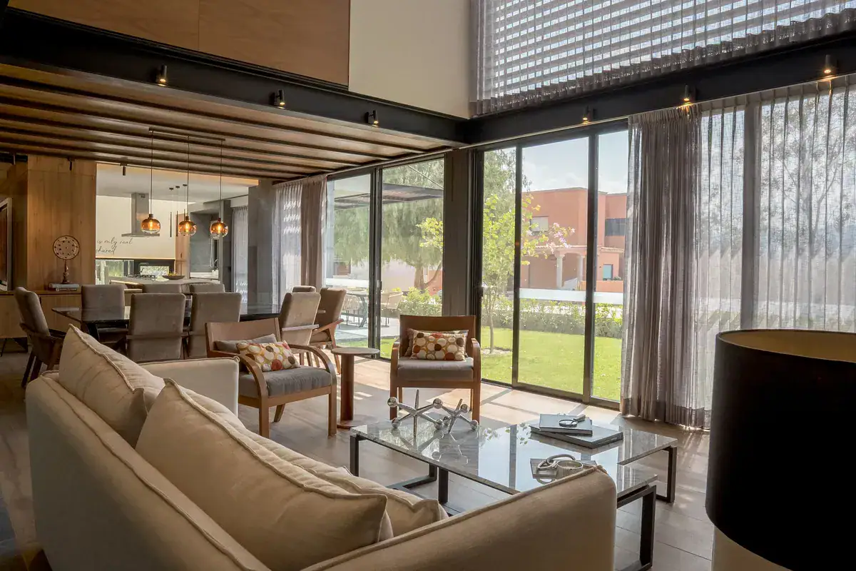 Bright House, living room with a beige sofa and a glass wall to the lawn beside the dining area, San Miguel de Allende