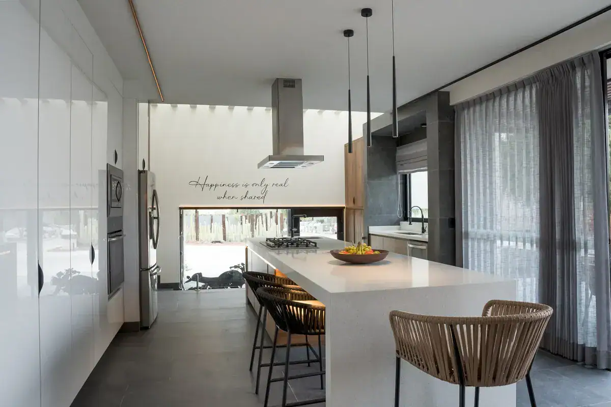 Bright House, kitchen with a white quartz island, wood-trimmed base, bar stools and a steel range hood, San Miguel de Allende