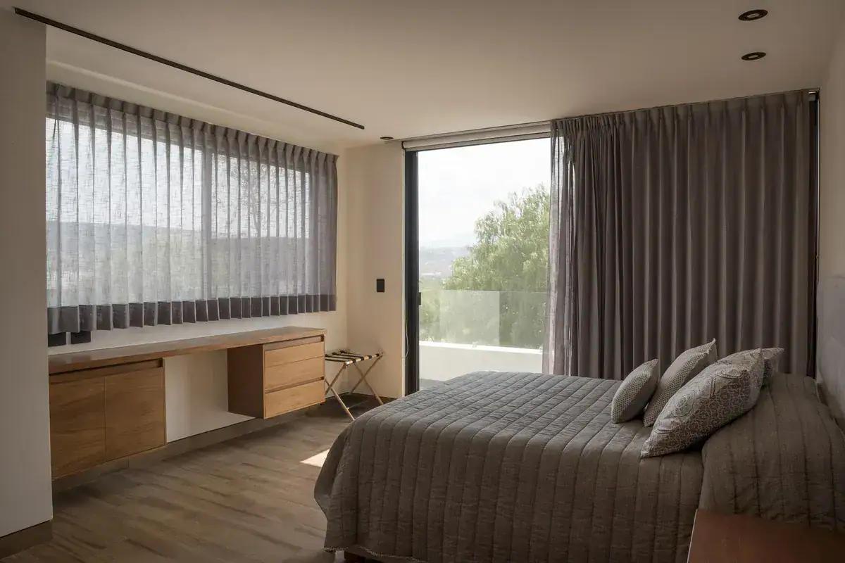 Bright House, bedroom with a built-in wood desk, a bed and a wide window with sheer curtains, San Miguel de Allende