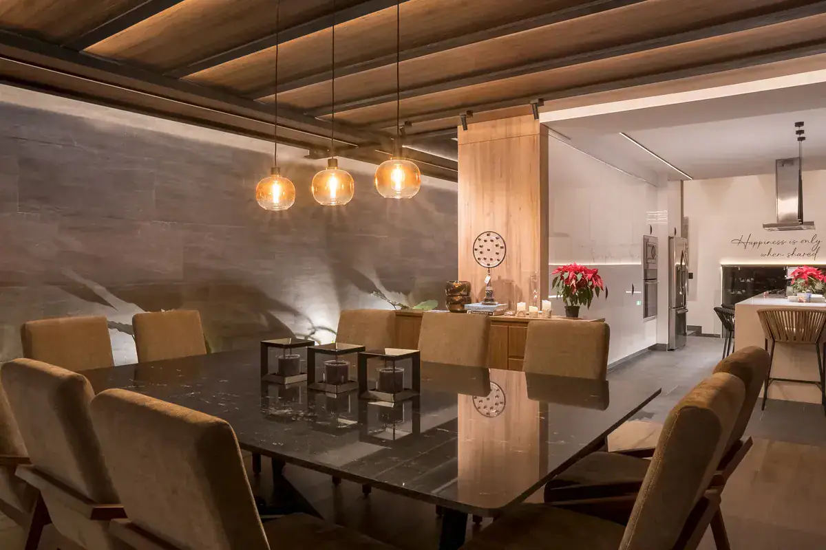Bright House, dining table with amber pendant lights and a wood panel wall in the evening, San Miguel de Allende