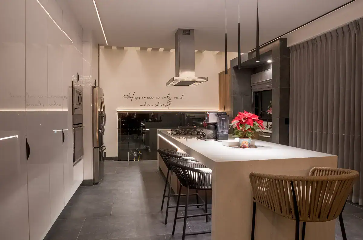Bright House, kitchen at night with a white island, bar stools and a Happiness is only real when shared wall script, San Miguel de Allende