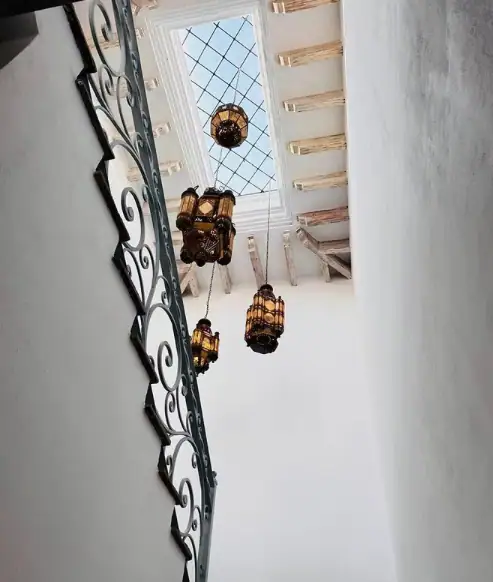 Interior stairwell viewed from below, featuring a decorative wrought-iron railing and hanging lanterns against white walls and a skylight above, San Miguel de Allende