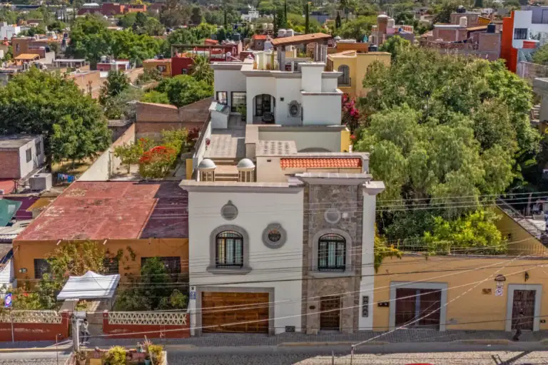 Casa 28 de Abril Norte, aerial view of the white three-story house with a rooftop terrace among trees and neighboring homes, San Miguel de Allende