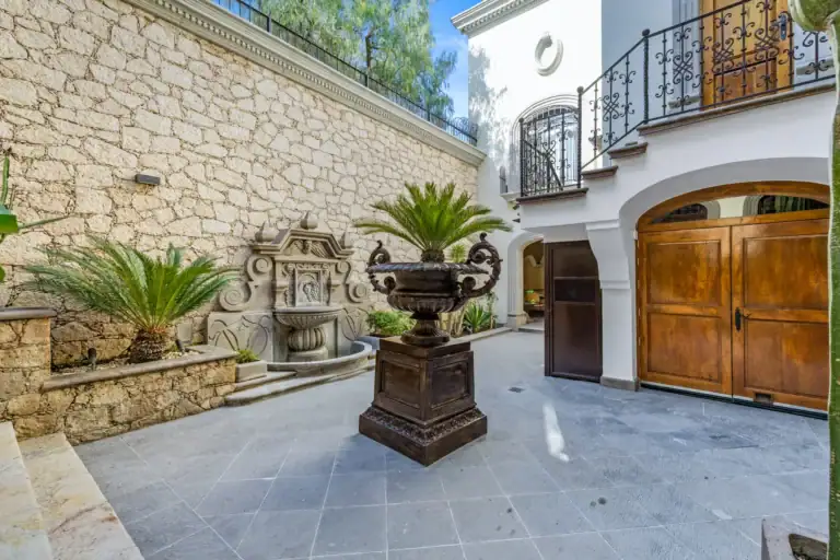 Casa 28 de Abril Norte, courtyard with a stone wall fountain, a large urn planter and wooden garage doors, San Miguel de Allende