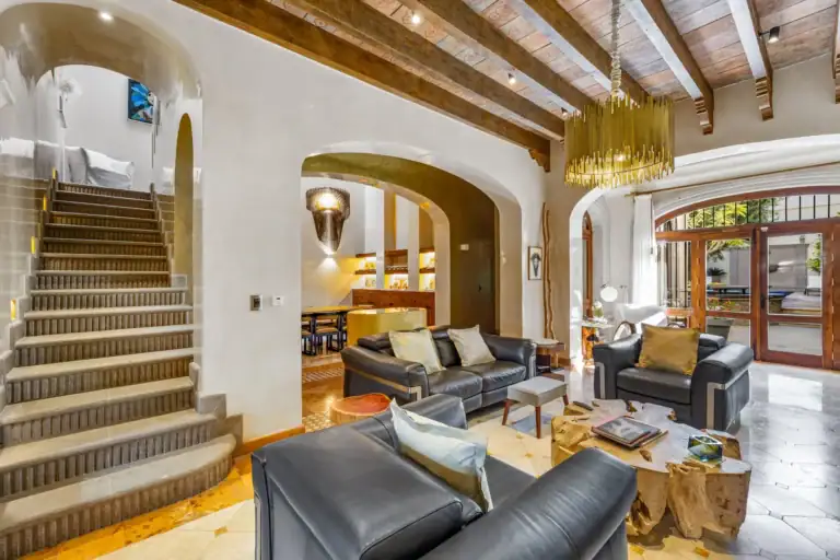 Casa 28 de Abril Norte, living room with black leather sofas, a root coffee table and a stone staircase under beamed ceilings, San Miguel de Allende