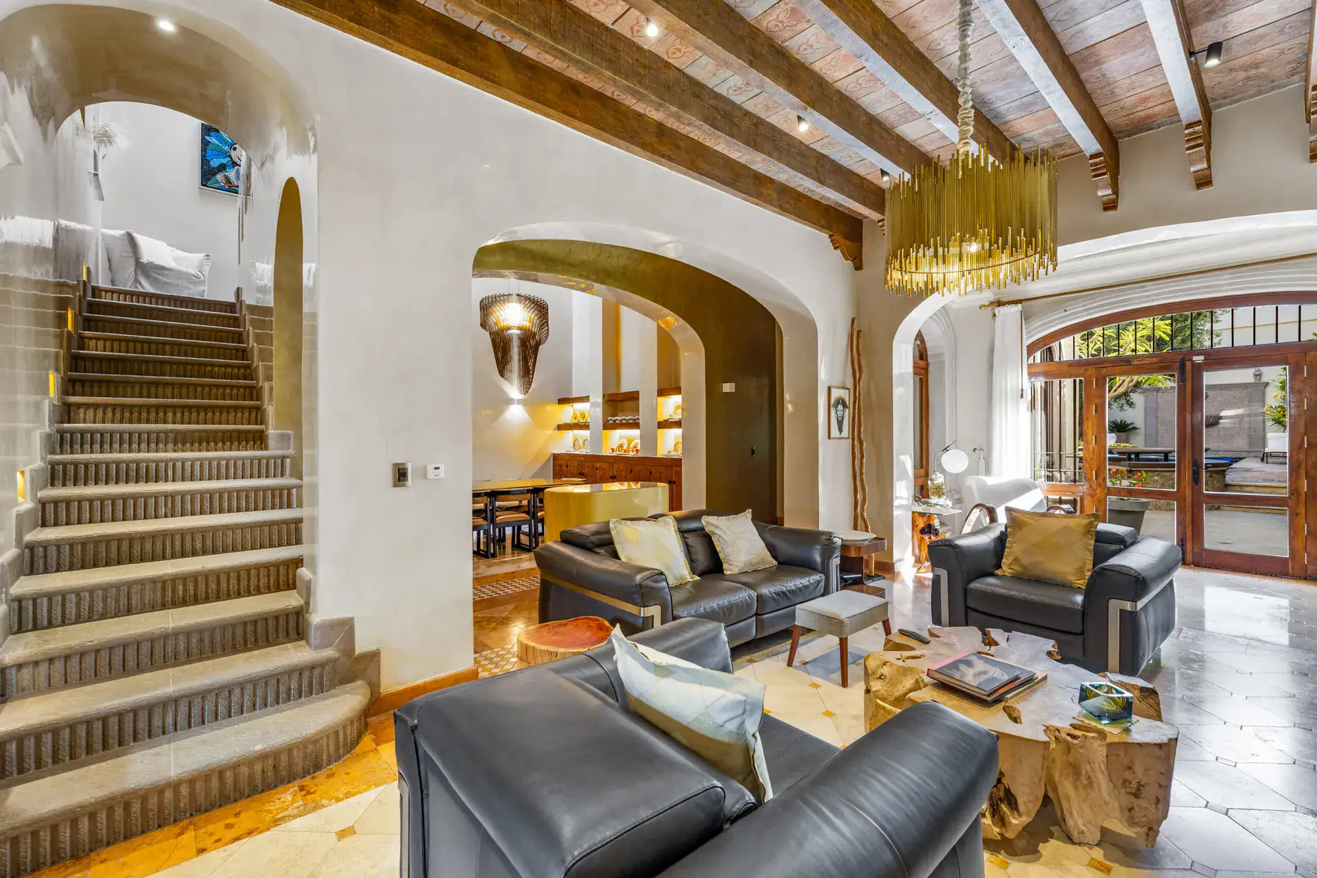 Casa 28 de Abril Norte, living room with black leather sofas, a root coffee table and a stone staircase under beamed ceilings, San Miguel de Allende