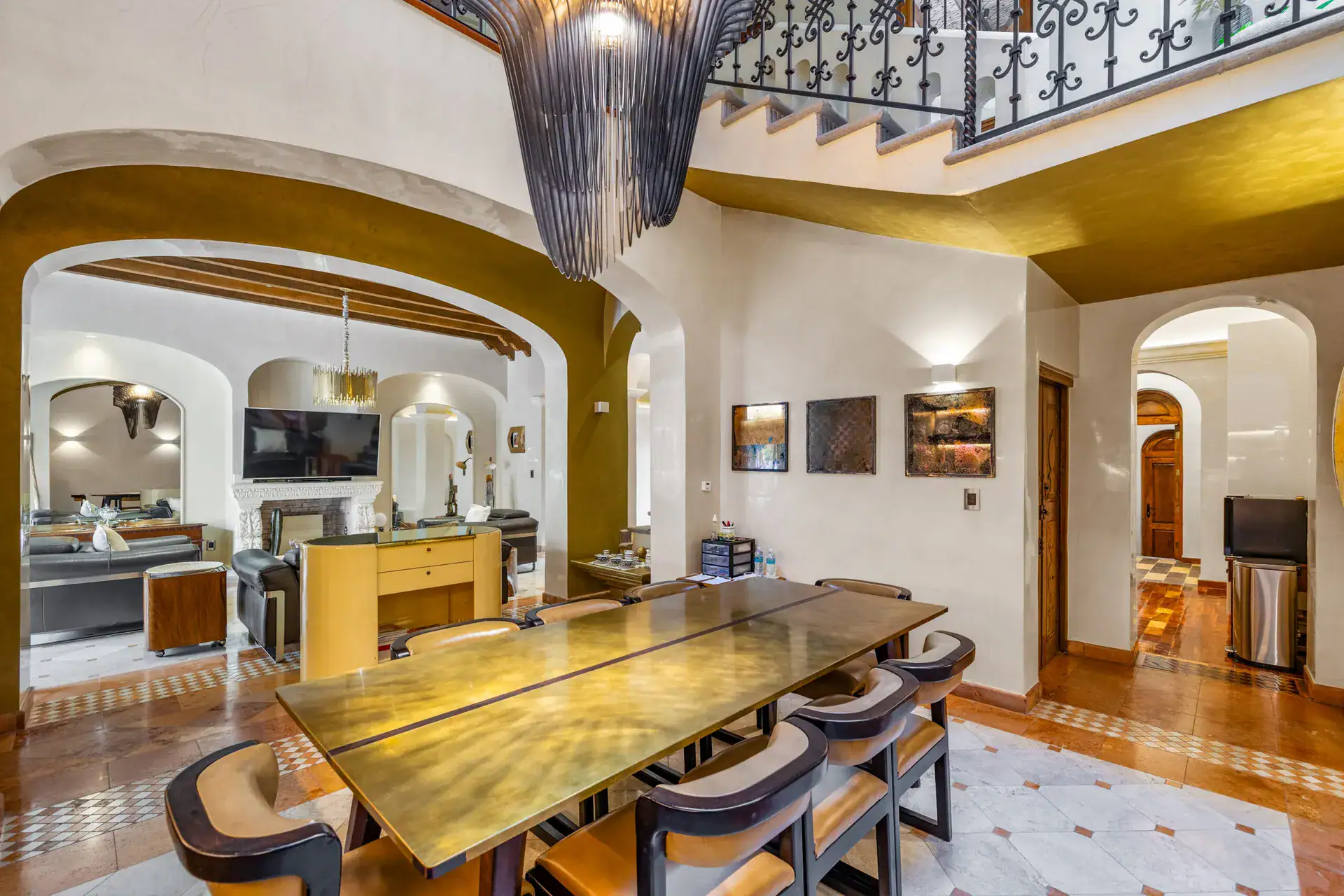 Casa 28 de Abril Norte, dining room with a long brass-topped table and a pendant chandelier open to the living room, San Miguel de Allende